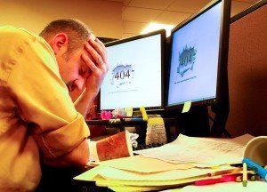 Man with head in hands at cluttered desk with 404 error on the computer